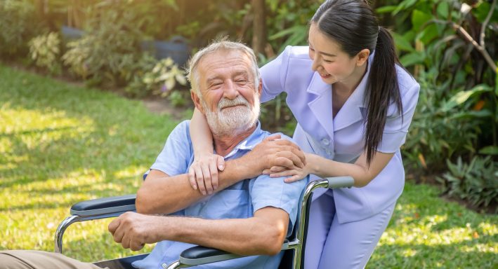 Happy nurse holding elderly man hand on wheelchair in garden at nursing home